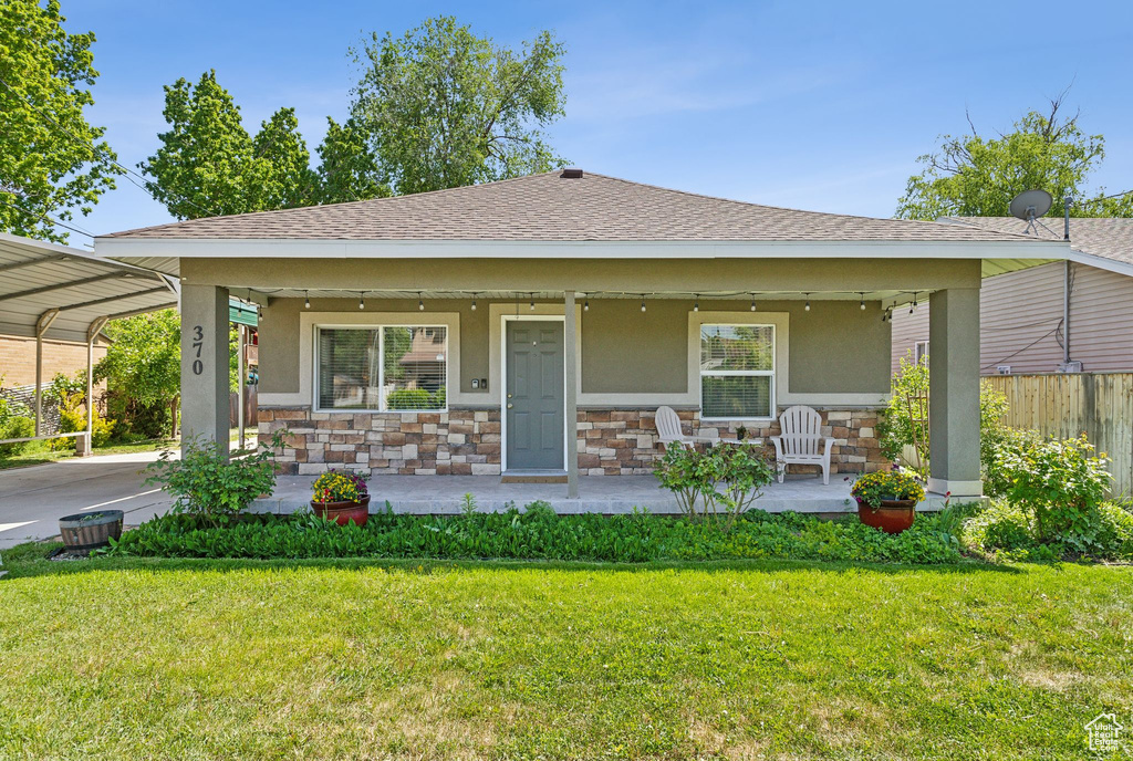 View of front of home featuring covered porch, stucco siding, stone siding, and a carport