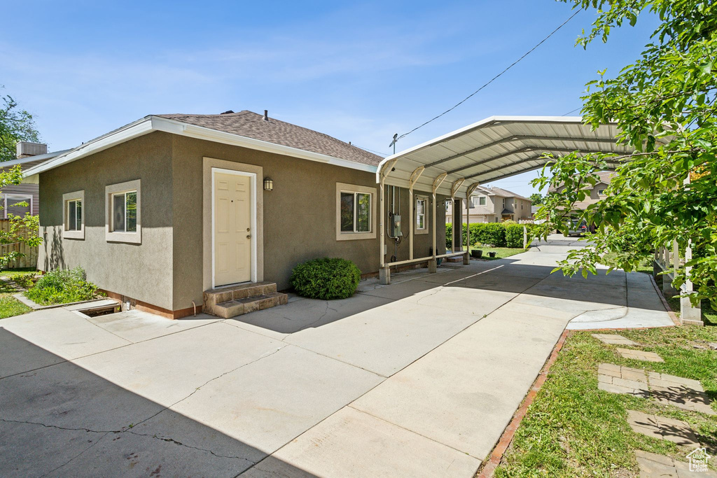 View of front of property featuring a carport, entry steps, stucco siding, and roof with shingles