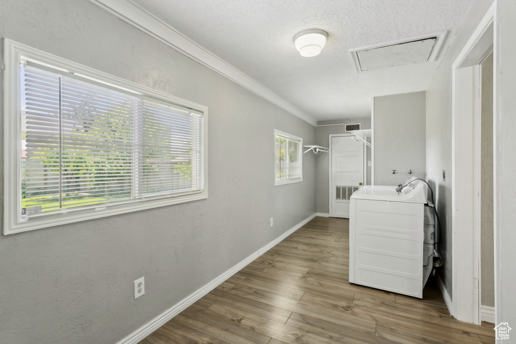 Laundry room with crown molding, wood finished floors, baseboards, and a textured ceiling