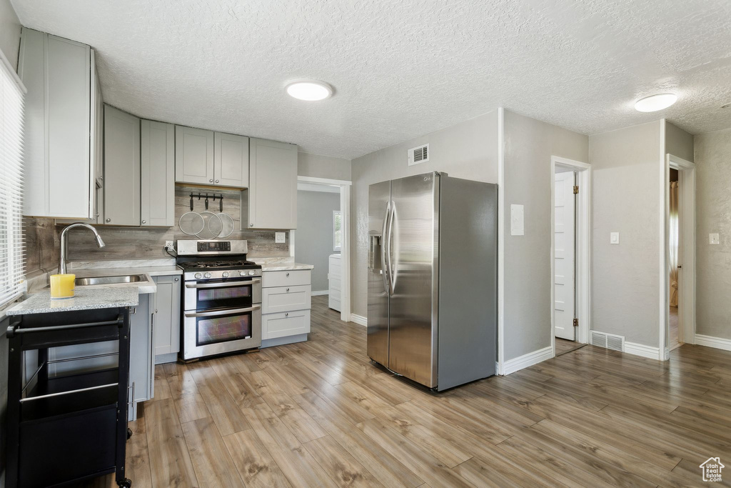 Kitchen featuring stainless steel appliances, gray cabinets, a sink, backsplash, and light wood-type flooring