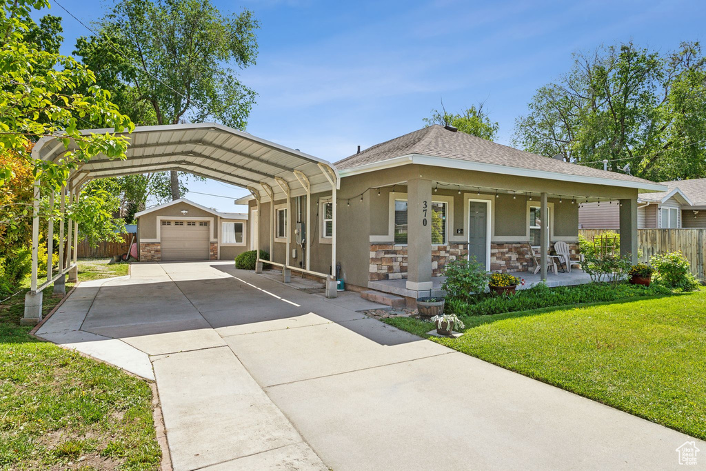 View of front of home featuring a detached carport, an outbuilding, concrete driveway, a porch, and stone siding
