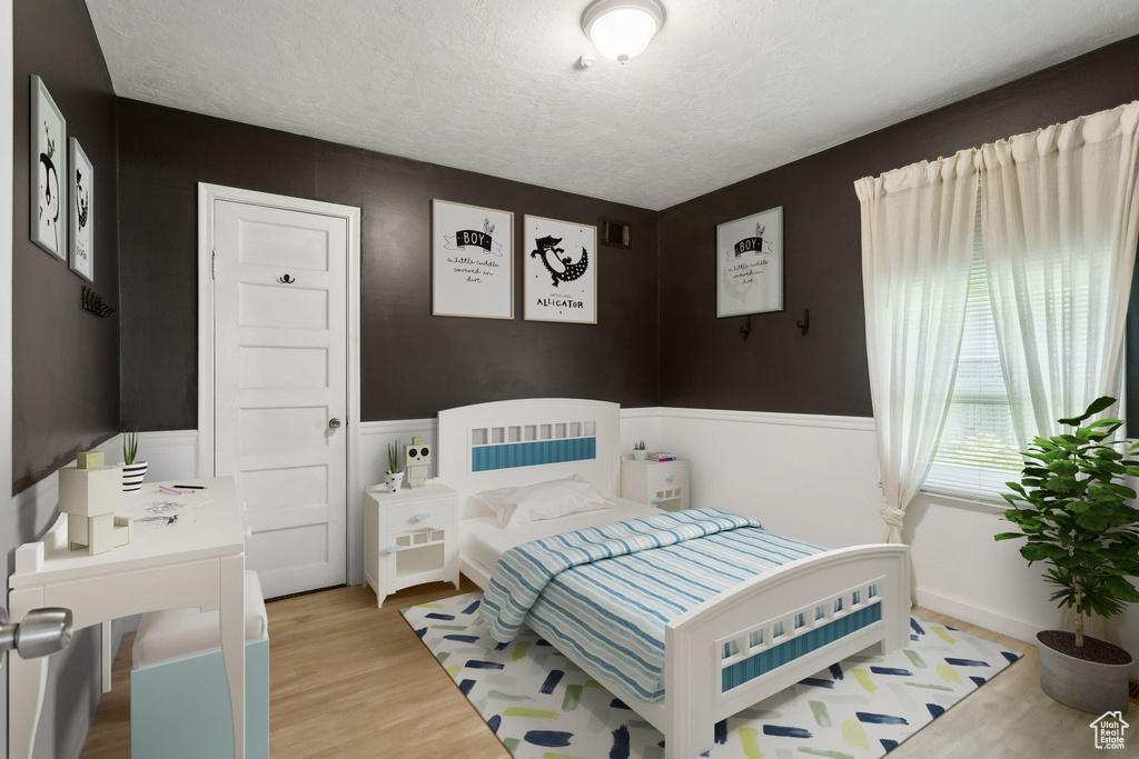 Bedroom with wood finished floors, a textured ceiling, and a wainscoted wall