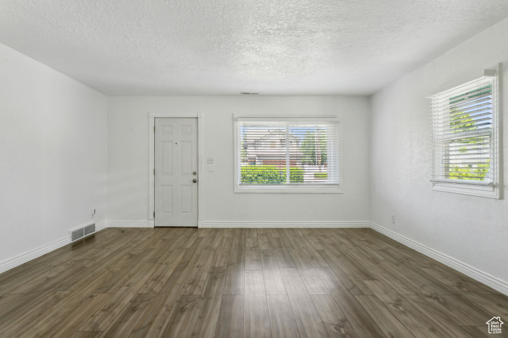 Unfurnished living room with a textured ceiling, dark wood-style flooring, and baseboards