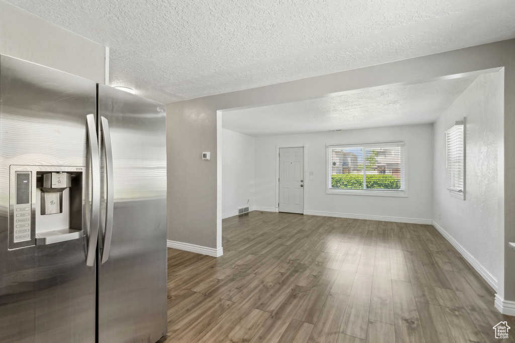 Unfurnished living room with a textured ceiling, wood finished floors, and baseboards