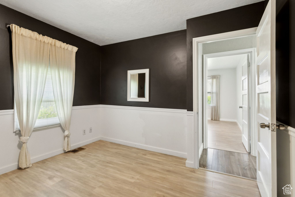 Empty room featuring plenty of natural light, light wood-style floors, a wainscoted wall, a textured ceiling, and baseboards