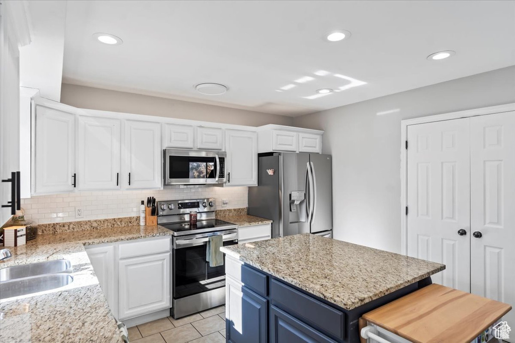 Kitchen featuring appliances with stainless steel finishes, blue cabinetry, tasteful backsplash, white cabinetry, and light tile patterned floors