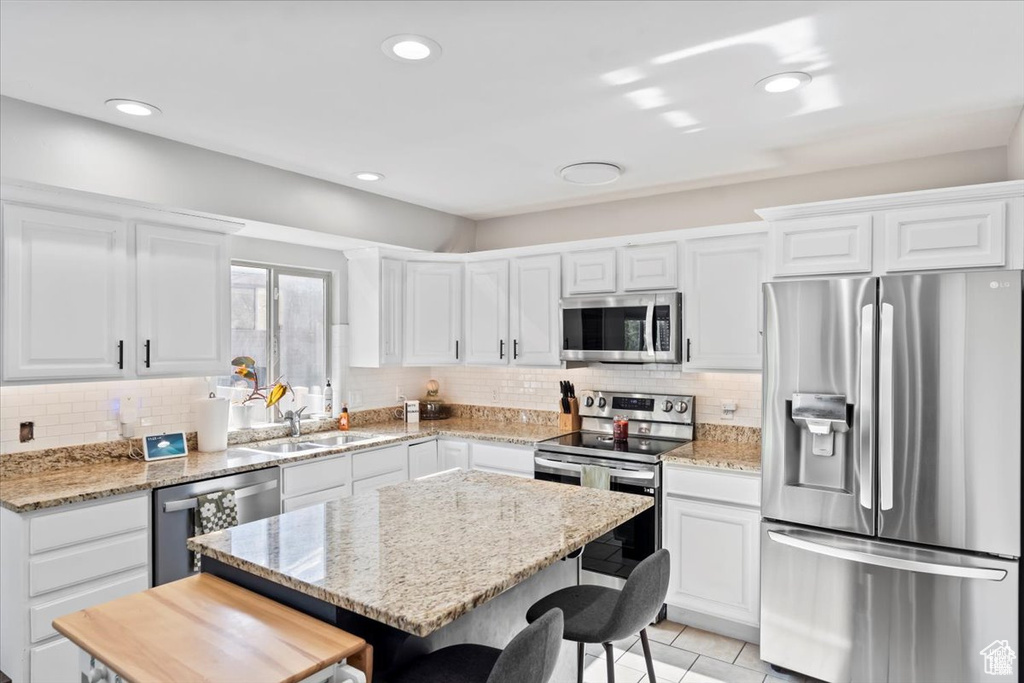 Kitchen featuring stainless steel appliances, a sink, a kitchen bar, white cabinetry, and recessed lighting