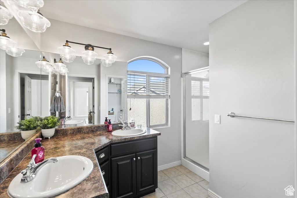 Full bathroom featuring a shower stall, tile patterned floors, baseboards, and double vanity