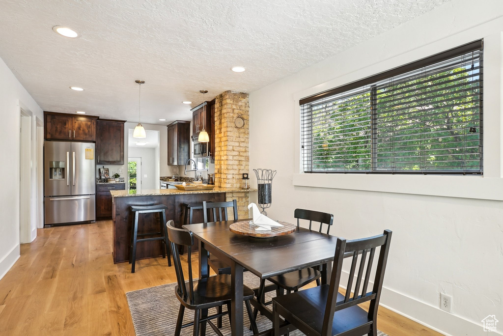 Dining space featuring light wood-style floors, a textured ceiling, baseboards, and recessed lighting