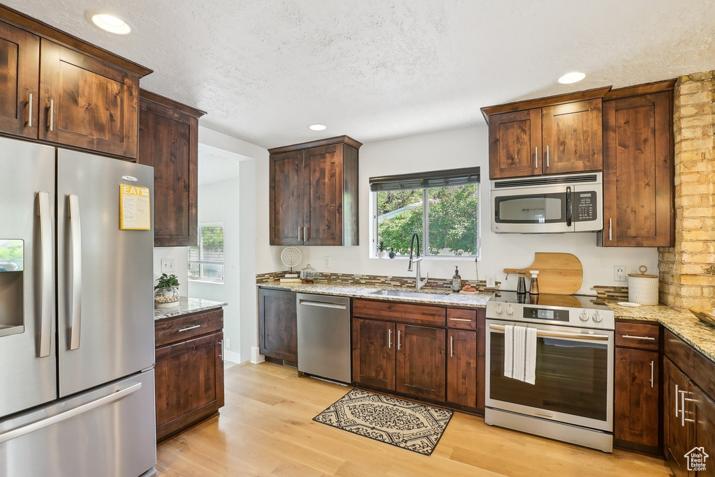Kitchen with appliances with stainless steel finishes, a sink, light stone counters, light wood-style flooring, and recessed lighting