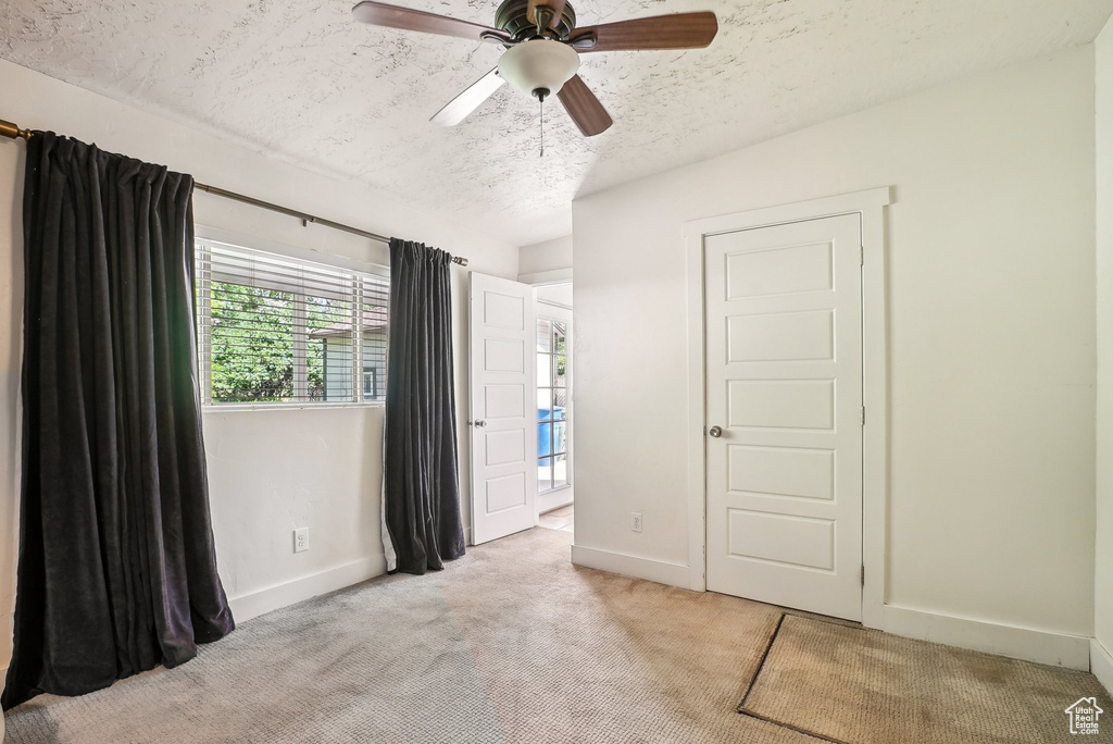 Unfurnished bedroom featuring a textured ceiling, light colored carpet, baseboards, and ceiling fan