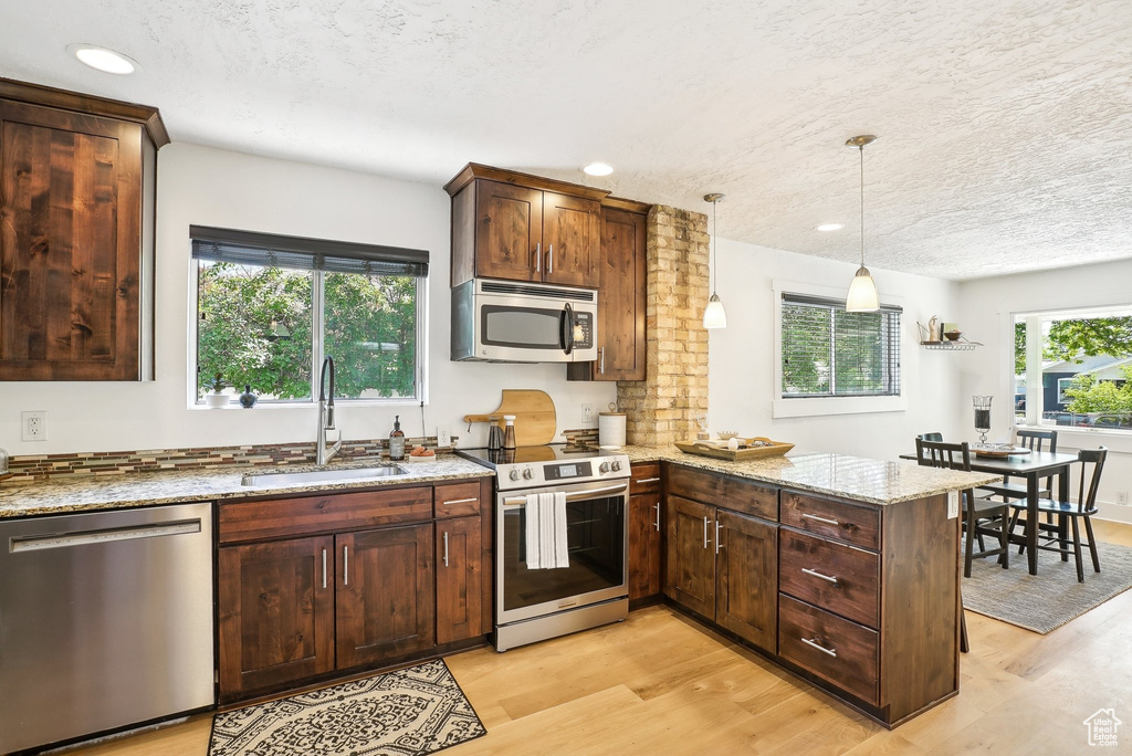 Kitchen featuring stainless steel appliances, a sink, a peninsula, light stone countertops, and light wood-style floors