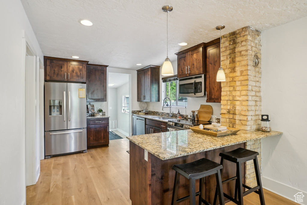 Kitchen featuring stainless steel appliances, light stone countertops, a sink, light wood finished floors, and baseboards