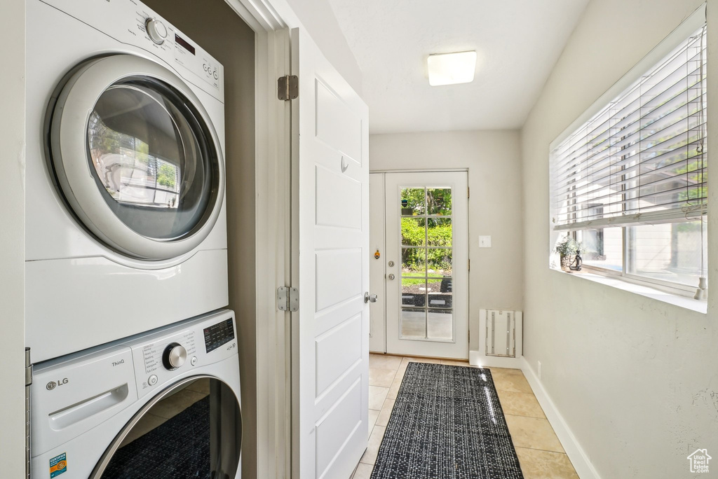 Laundry room with stacked washer and clothes dryer, light tile patterned floors, and baseboards