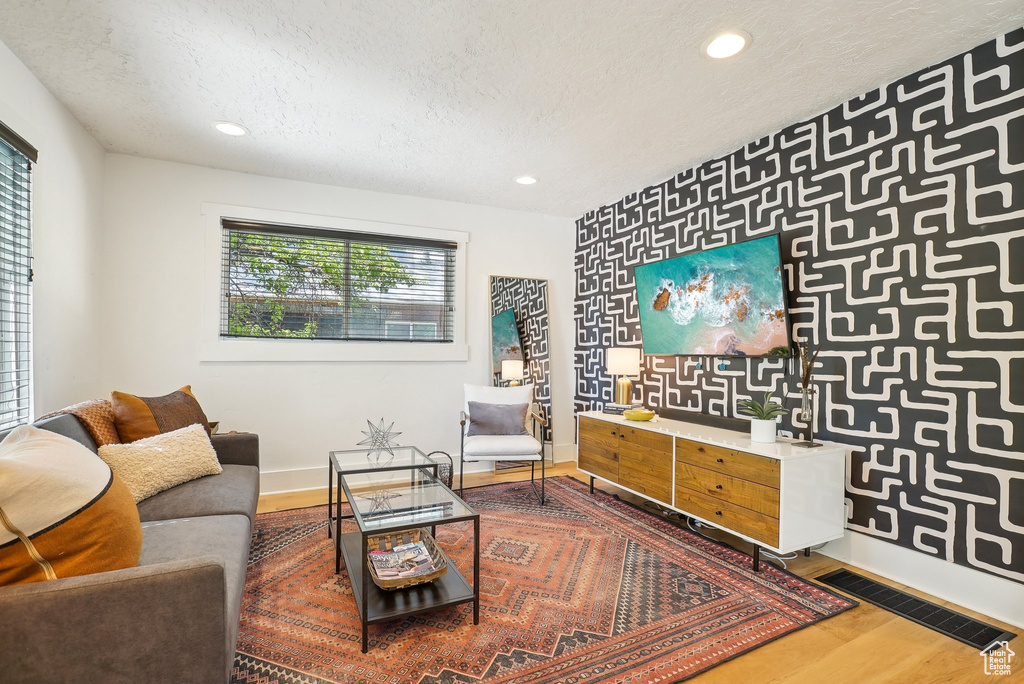 Living area featuring baseboards, a textured ceiling, wood finished floors, recessed lighting, and an accent wall