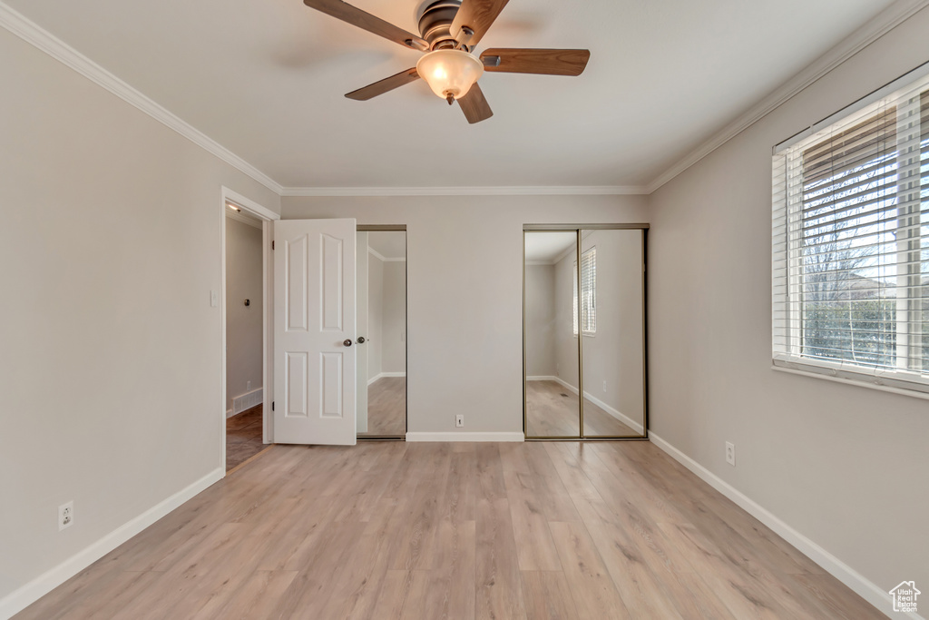 Unfurnished bedroom with two closets, light wood-style floors, baseboards, crown molding, and a ceiling fan