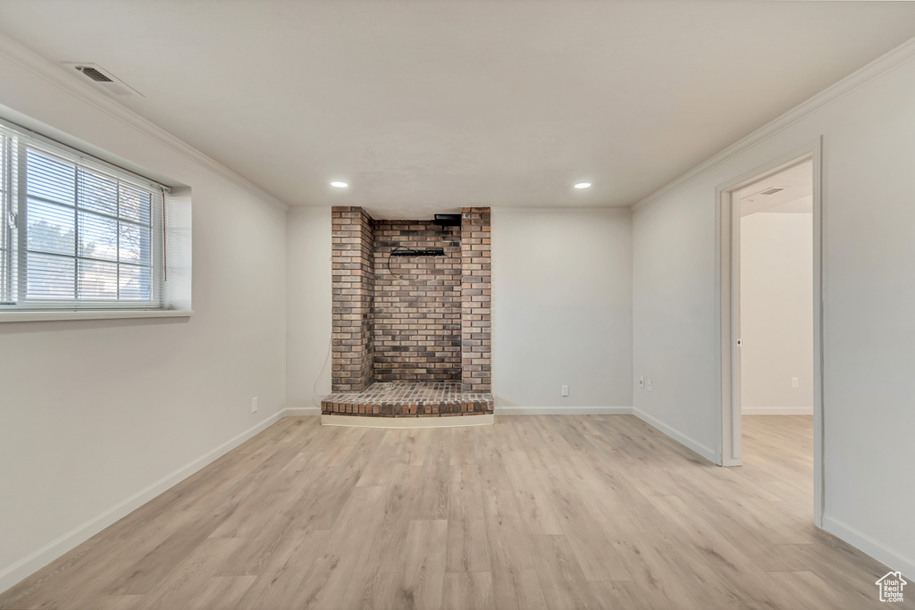 Unfurnished living room featuring wood finished floors, crown molding, recessed lighting, baseboards, and a brick fireplace