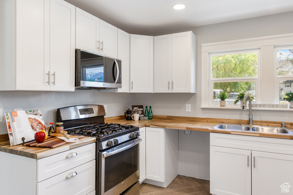 Kitchen with stainless steel appliances, a sink, butcher block countertops, white cabinetry, and recessed lighting
