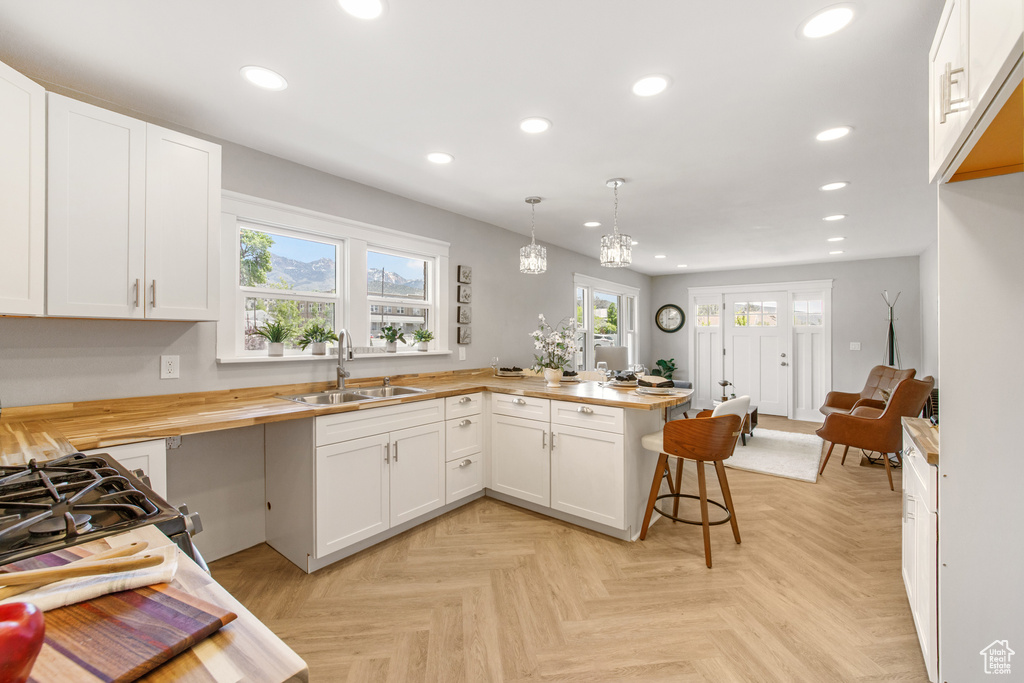 Kitchen featuring a sink, wooden counters, a peninsula, recessed lighting, and white cabinetry