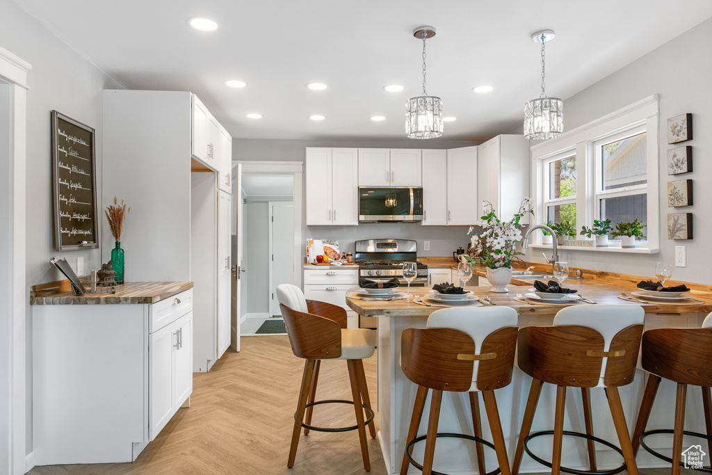 Kitchen featuring appliances with stainless steel finishes, a breakfast bar, recessed lighting, decorative light fixtures, and white cabinetry