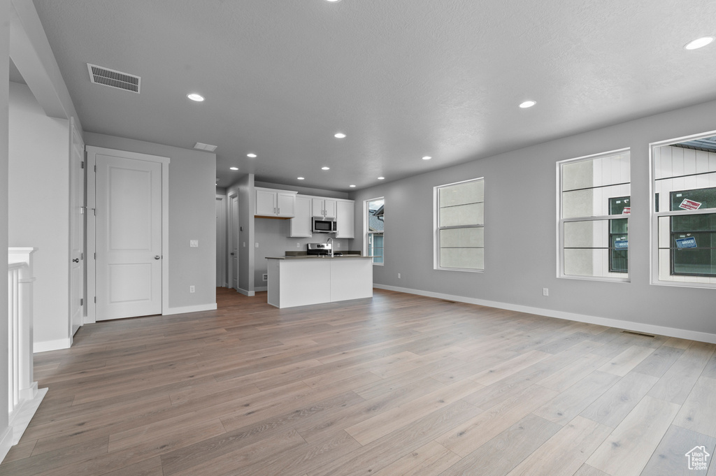 Unfurnished living room with light wood-type flooring, baseboards, and recessed lighting