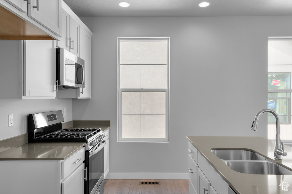 Kitchen featuring stainless steel appliances, a sink, stainless steel countertops, light wood-style flooring, and white cabinetry