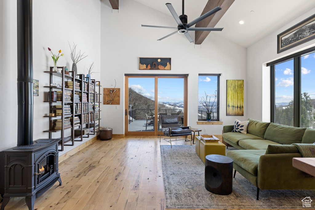 Living area with high vaulted ceiling, ceiling fan, light wood-style floors, a wood stove, and baseboards