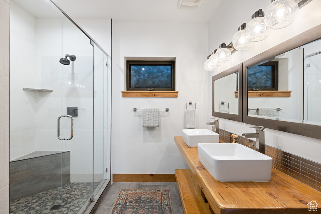 Bathroom featuring a stall shower, double vanity, and baseboards