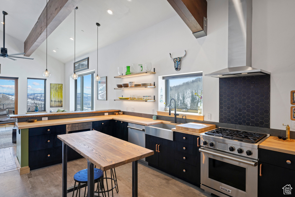 Kitchen with dark cabinets, luxury stove, butcher block countertops, a sink, and wall chimney range hood