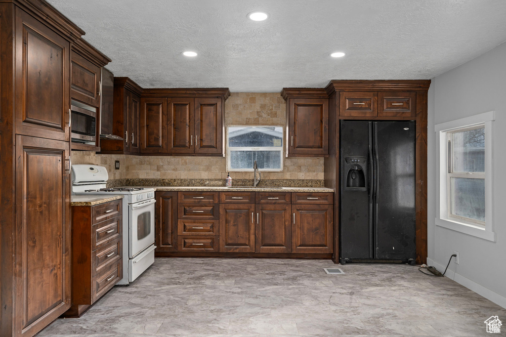 Kitchen featuring black fridge, white range with gas stovetop, stainless steel microwave, a sink, and decorative backsplash