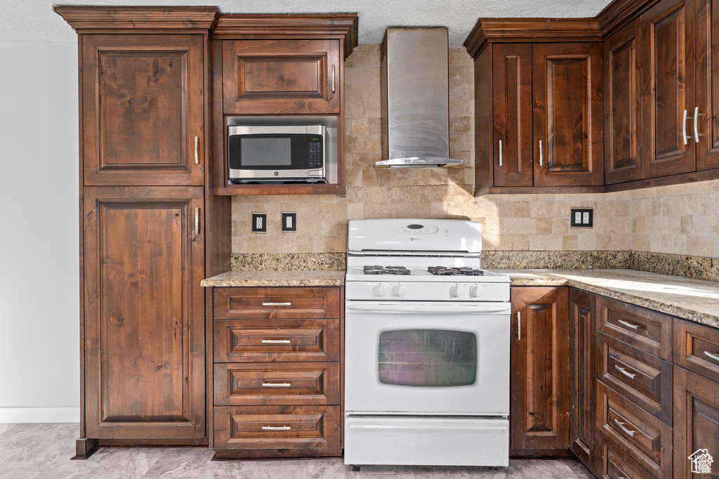 Kitchen featuring gas range gas stove, wall chimney exhaust hood, stainless steel microwave, dark brown cabinetry, and tasteful backsplash