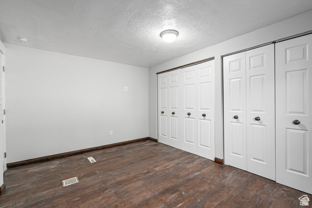 Unfurnished bedroom with multiple closets, dark wood-style floors, baseboards, and a textured ceiling