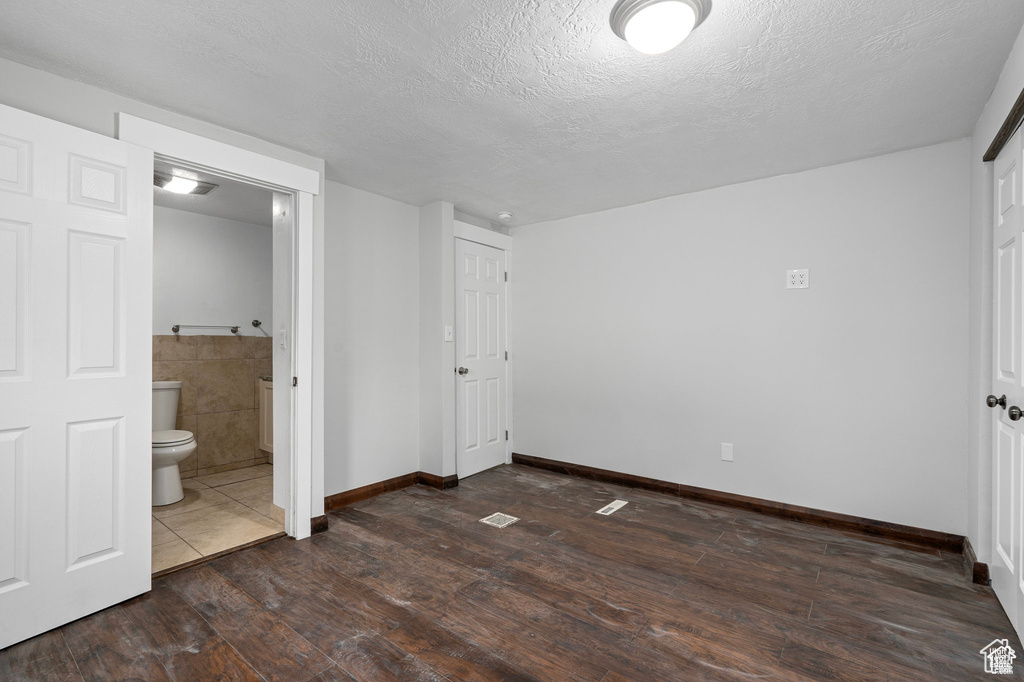 Unfurnished bedroom with dark wood-style floors, a textured ceiling, ensuite bath, and baseboards