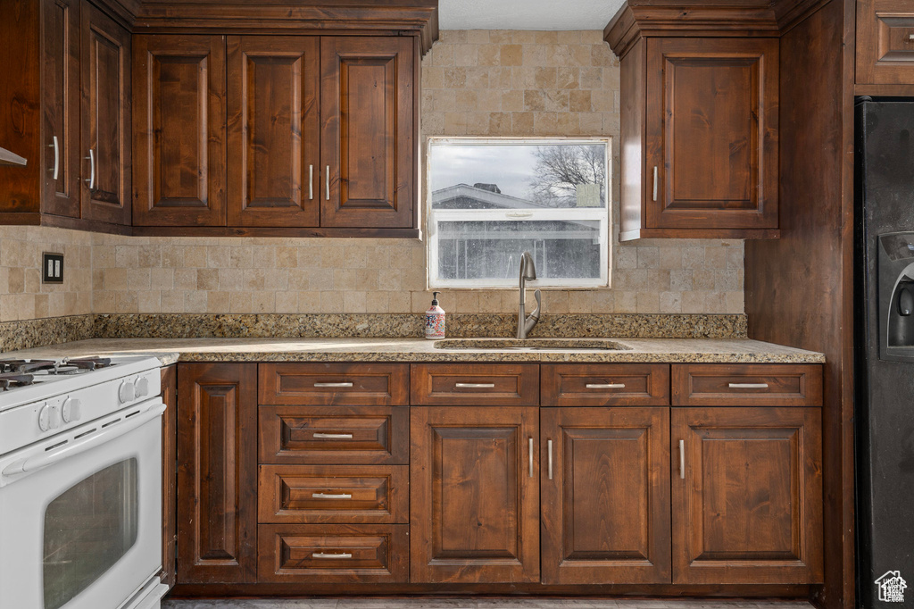 Kitchen with white range with gas cooktop, a sink, backsplash, and light countertops
