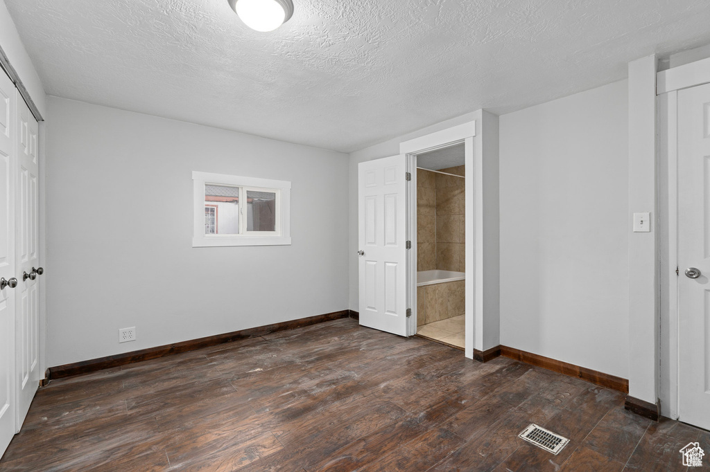 Unfurnished bedroom with baseboards, dark wood-style flooring, a textured ceiling, a closet, and ensuite bath