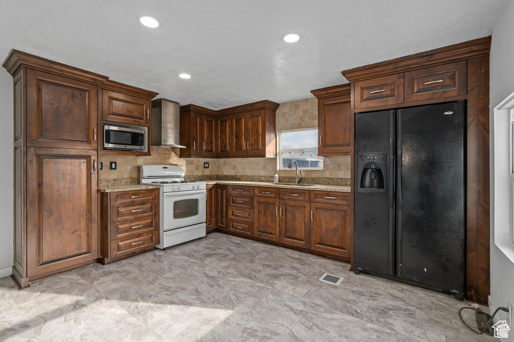 Kitchen with black fridge, white range with gas cooktop, stainless steel microwave, a sink, and wall chimney range hood