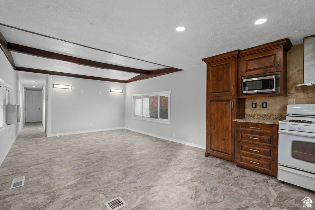 Kitchen with white gas range, stainless steel microwave, a textured ceiling, beamed ceiling, and baseboards
