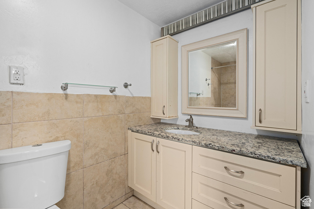 Bathroom with tile walls, vanity, toilet, and a textured ceiling
