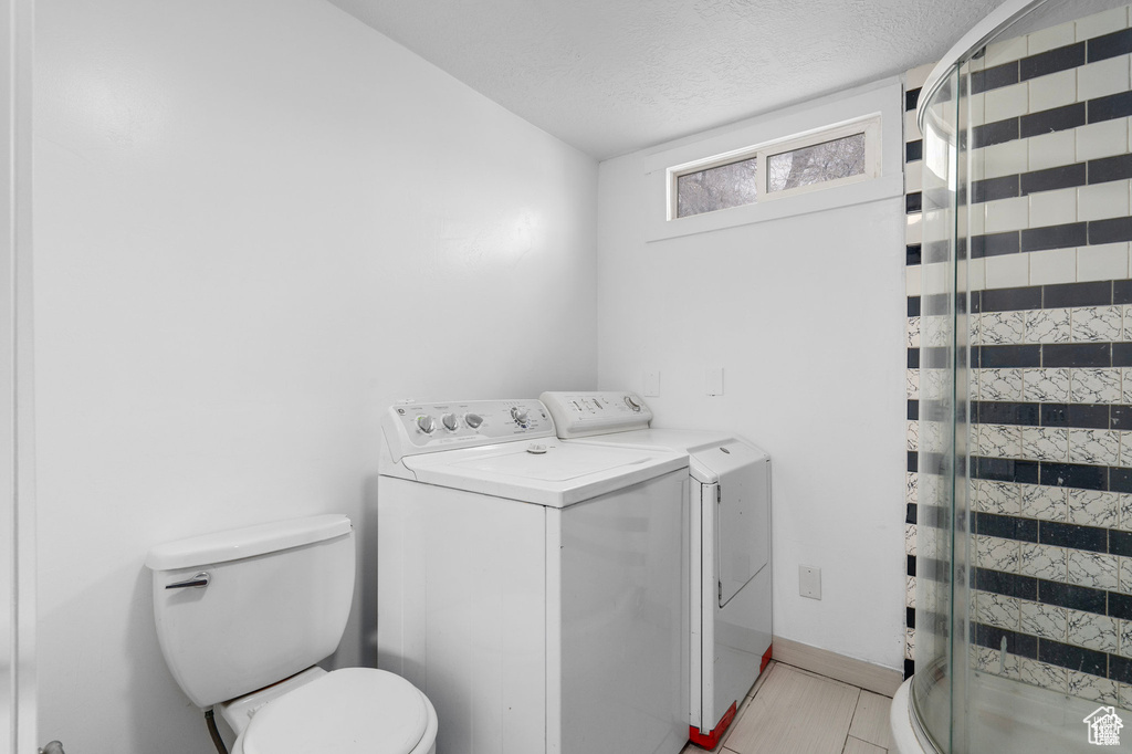 Washroom featuring washing machine and dryer, a textured ceiling, and light tile patterned floors