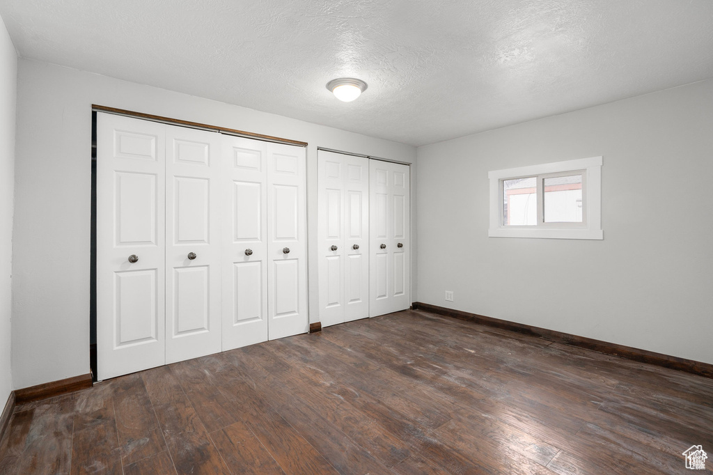 Unfurnished bedroom with multiple closets, baseboards, dark wood-type flooring, and a textured ceiling