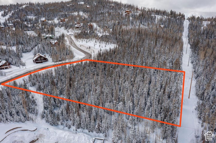 Snowy aerial view featuring property parcel outlined, a view of trees, and a mountain view