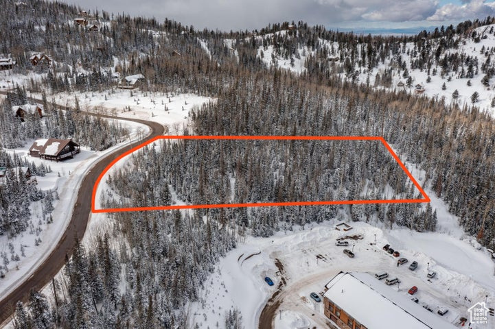 Snowy aerial view featuring a mountain view, property boundaries highlighted, and a view of trees