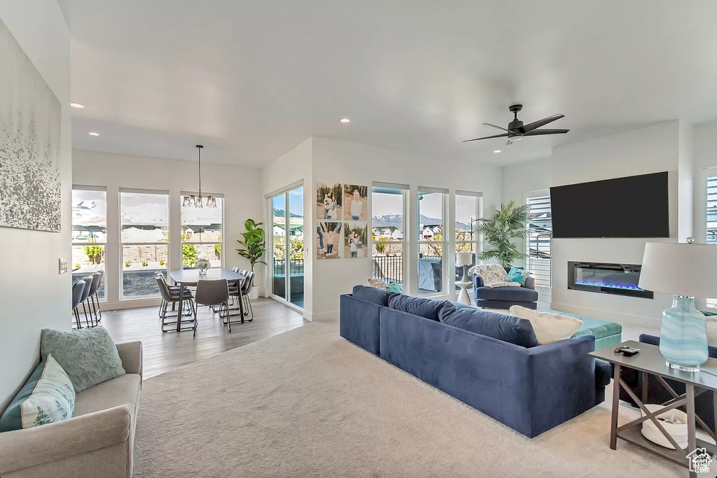 Living room featuring recessed lighting, a ceiling fan, a glass covered fireplace, a chandelier, and light wood-type flooring