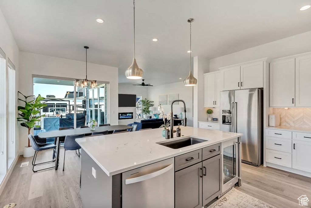 Kitchen featuring stainless steel appliances, a sink, light wood-type flooring, tasteful backsplash, and beverage cooler
