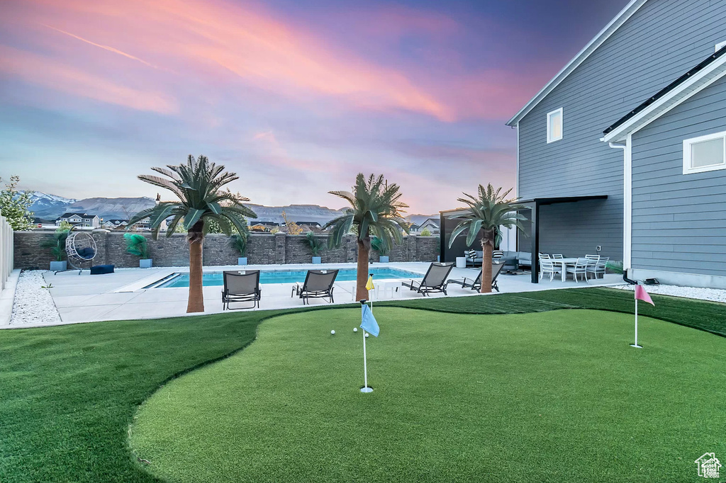 Yard at dusk featuring a putting area, a patio, and a fenced backyard