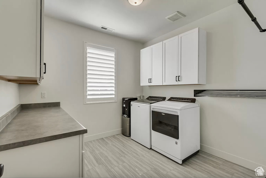 Laundry area featuring independent washer and dryer, cabinet space, and baseboards