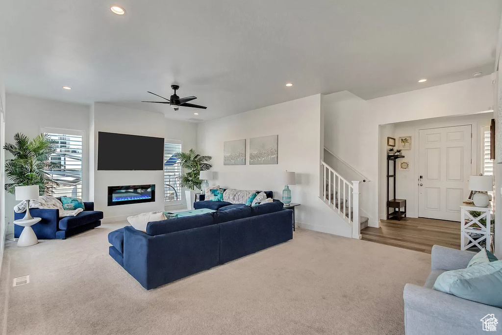 Carpeted living room featuring stairs, ceiling fan, recessed lighting, and a glass covered fireplace