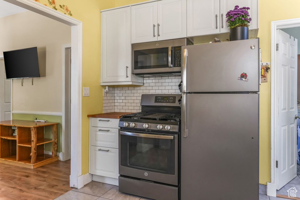 Kitchen with stainless steel appliances, white cabinetry, backsplash, and wood counters