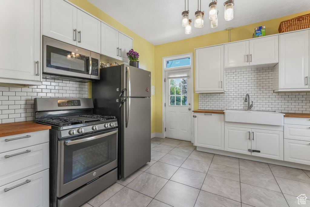 Kitchen with stainless steel appliances, wood counters, a sink, white cabinets, and decorative backsplash