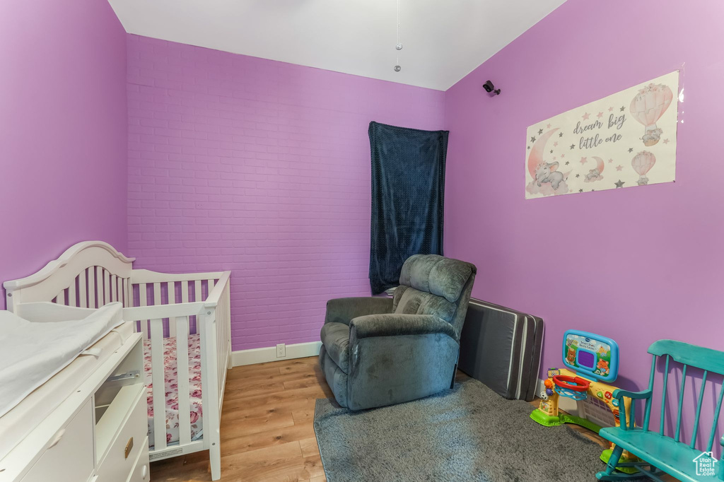 Bedroom featuring wood finished floors, a crib, and brick wall